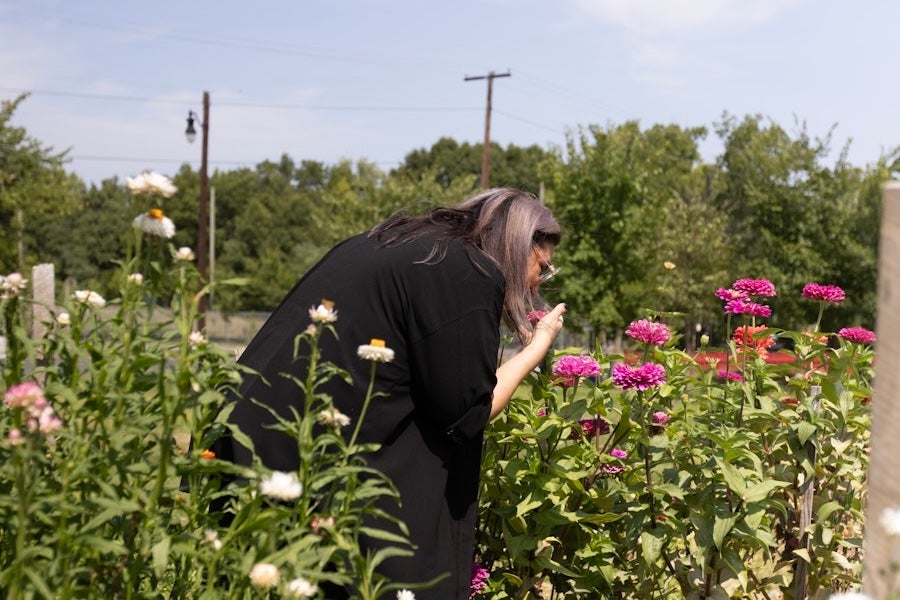 A woman leans in to smell pink flowers in a sunlit garden.