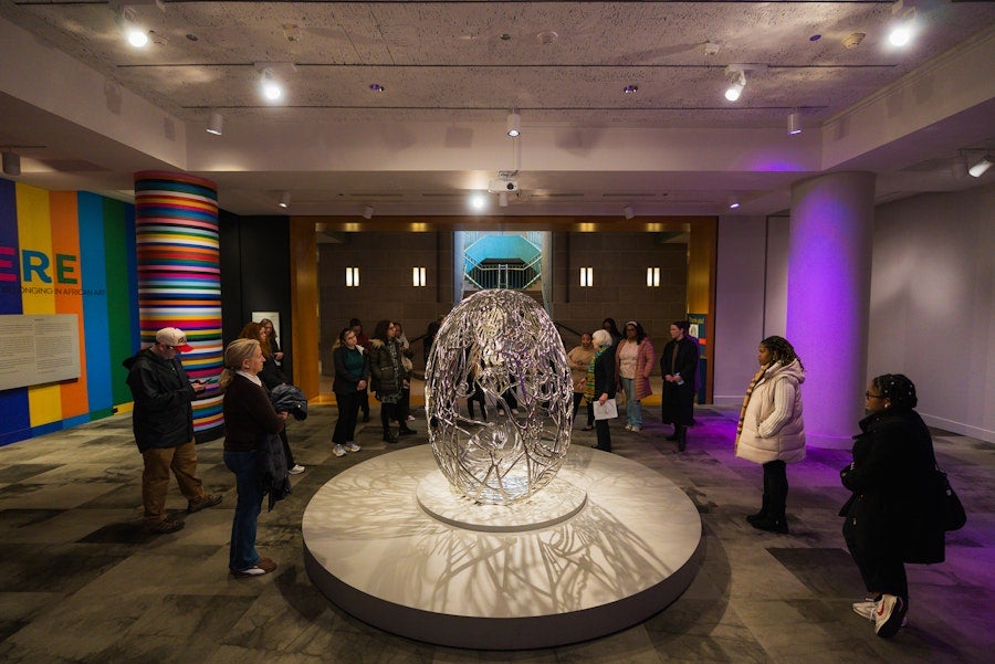 People viewing a large sphere sculpture in a gallery with colorful wall panels
