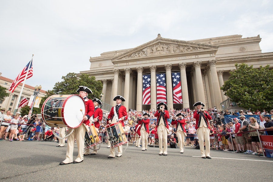 Revolutionary War reenactors drumming and marching in a parade before a large building