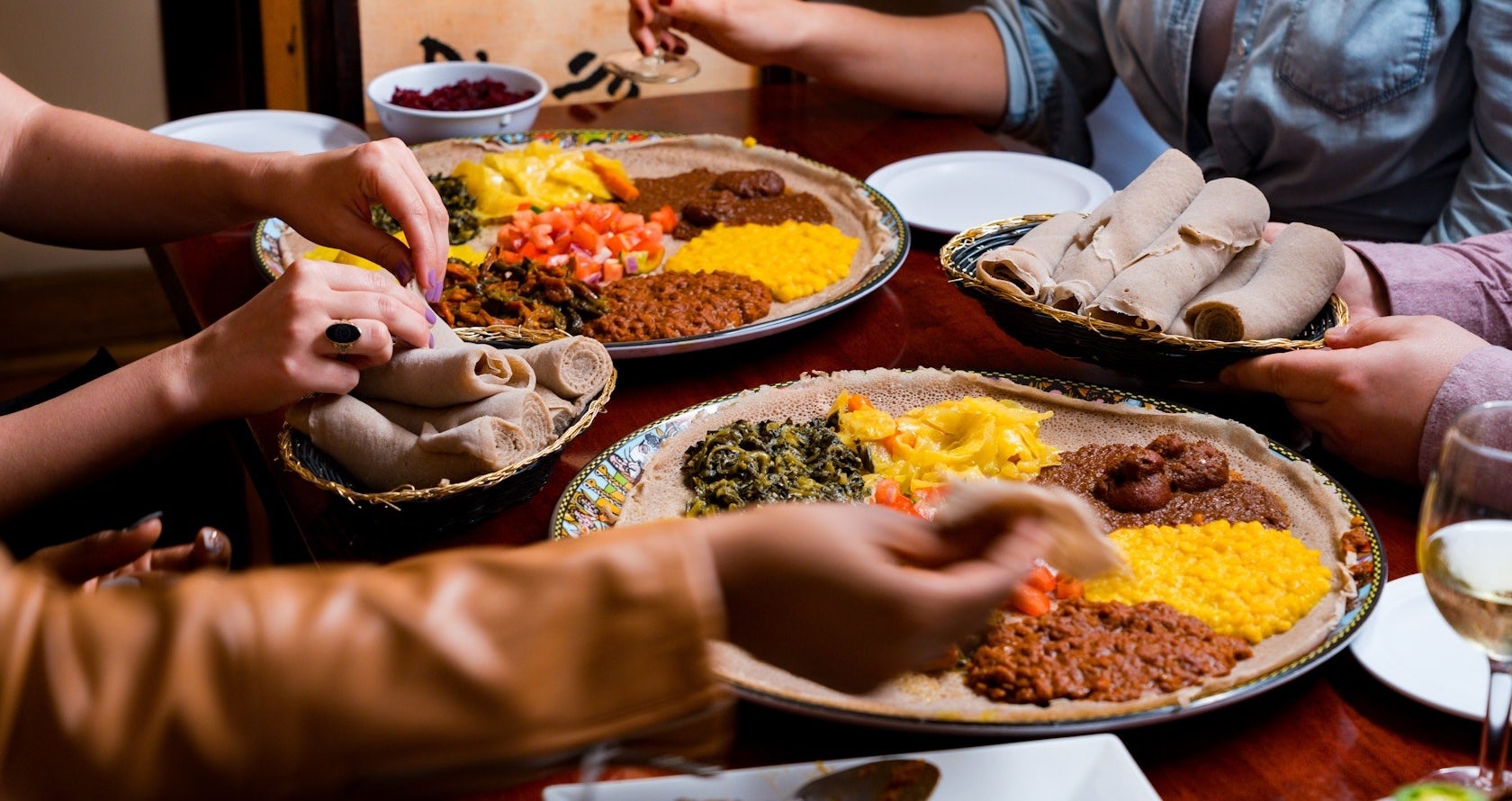 Hands sharing Ethiopian injera platter with stews