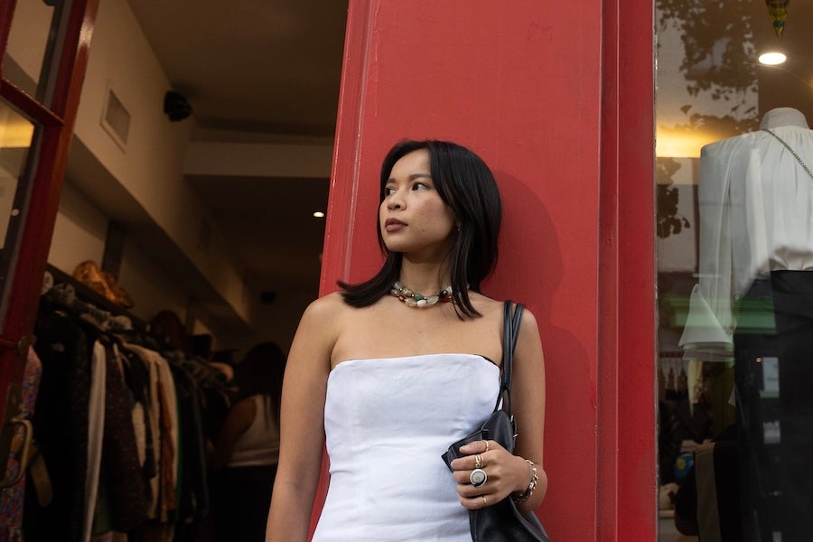 Woman in strapless white top standing by red doorway, looking left