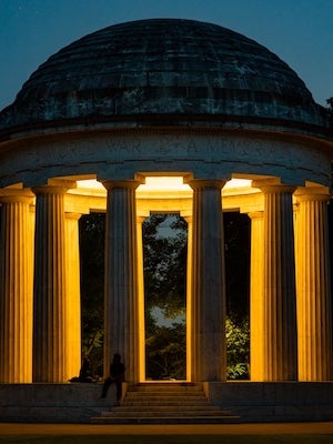 Illuminated domed pavilion with columns at dusk, warm yellow lights and a person seated inside