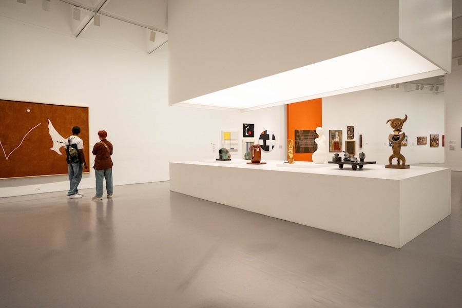 Two people viewing art and sculptures in a modern gallery with white walls
