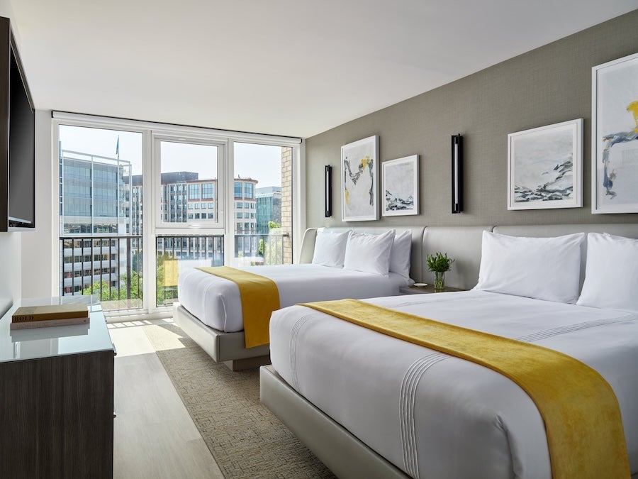 Modern hotel room with two beds and city view through large windows