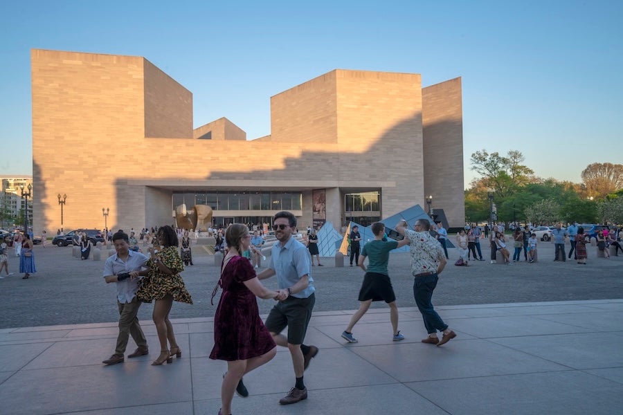 People walking in a plaza outside a modern beige stone building at dusk