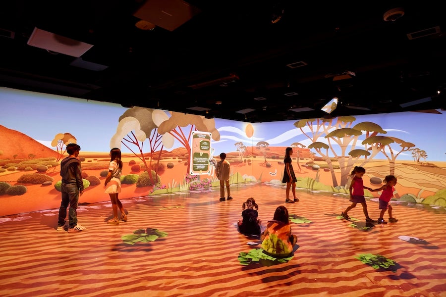People standing and sitting in a virtual desert landscape under a curved screen display