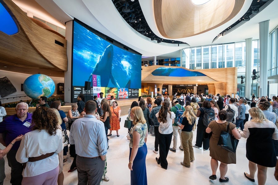 Crowd gathered in a modern atrium with large screens and a globe display