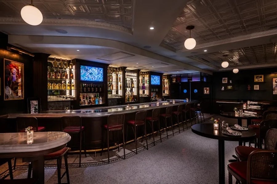 Dimly lit bar with high-top tables and long row of stools