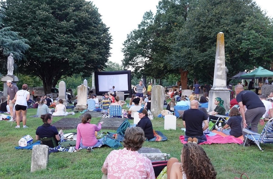 People seated on blankets and chairs at an outdoor movie screening in the Congressional Cemetary