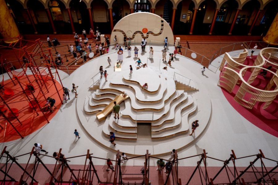 Overhead view of visitors exploring a sculptural, tiered climbing structure at the National Building Museum’s PLAYGROUND exhibition.