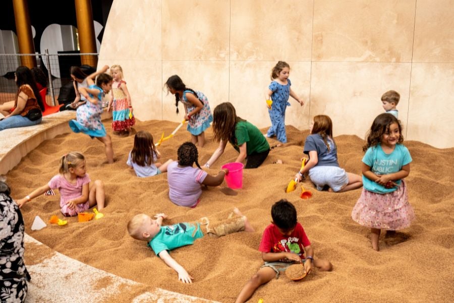 Children digging, building and playing in a large indoor sand pit at the National Building Museum’s PLAYGROUND exhibition.