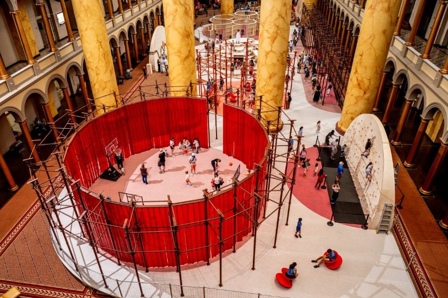 Wide view of the National Building Museum’s Great Hall transformed by the interactive PLAYGROUND exhibition, featuring climbing structures, play areas and hands-on installations.