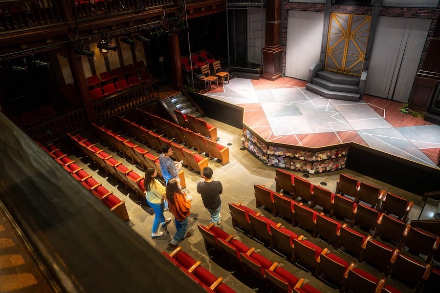 Empty Folger Shakespeare Library Theater with red seats and people walking down an aisle toward the stage
