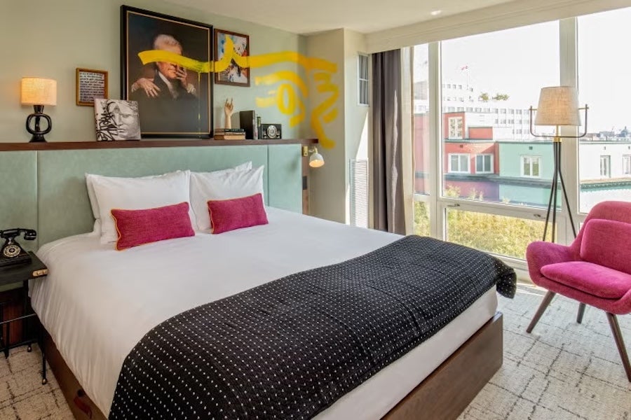 Photo of bright bedroom with king bed, pink pillows and chair, balcony view through large windows