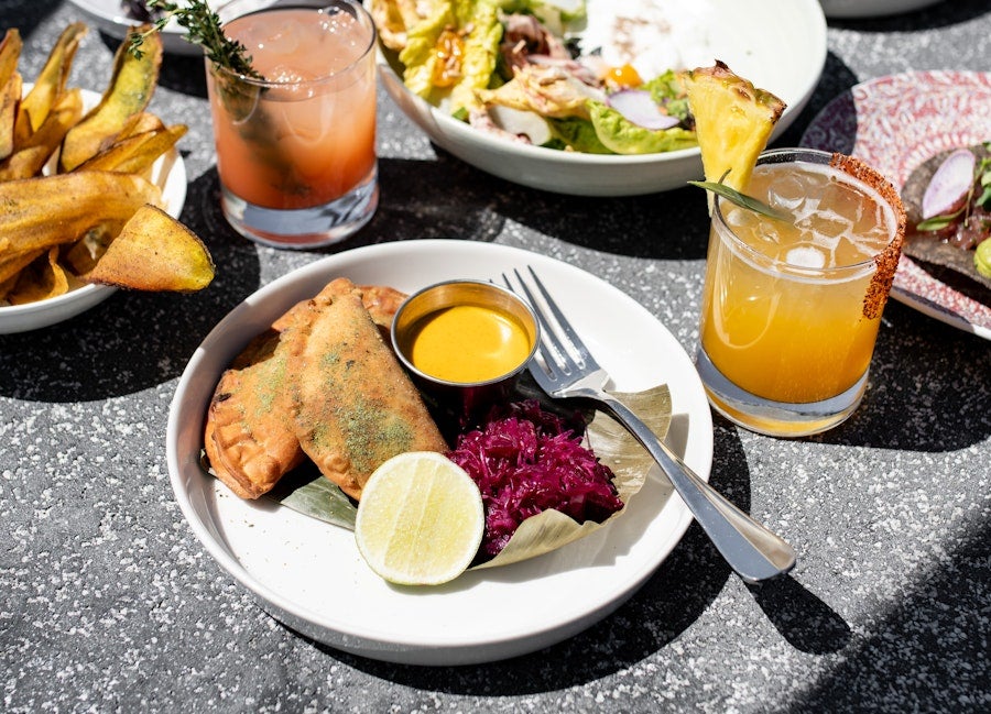 Plates of empanadas and salad with citrus drinks on a sunny patio table