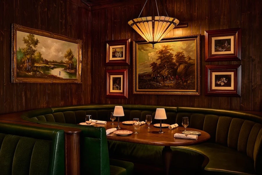Dimly lit restaurant booth with framed art and set dining tables under a warm lamp