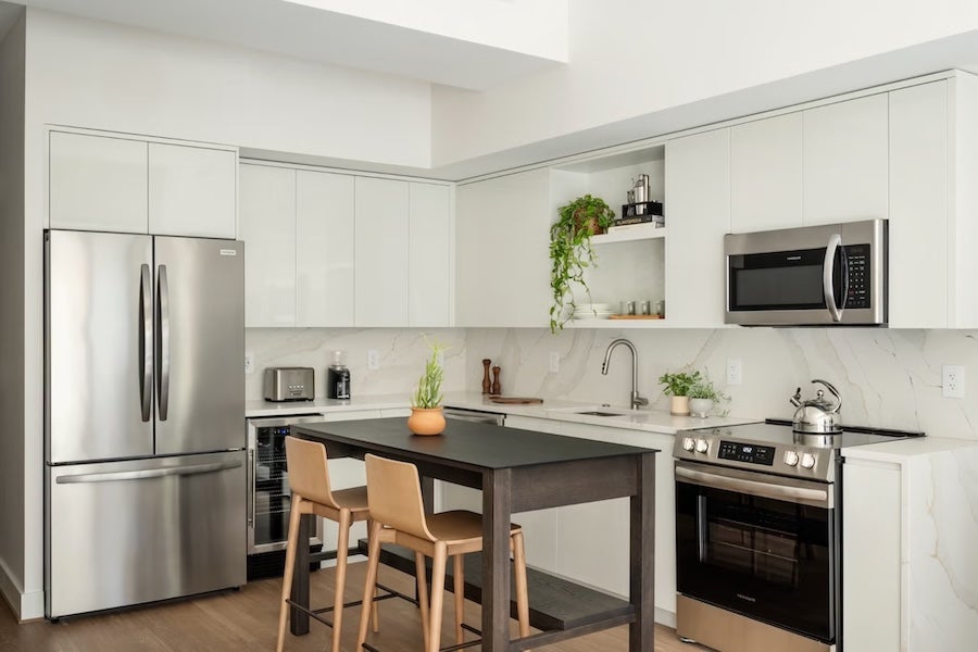 Modern white kitchen with stainless steel appliances and island with two wooden stools