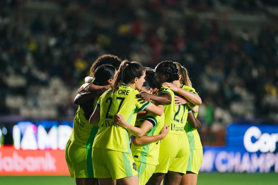 Group of soccer players in neon green jerseys huddle on the field in a stadium