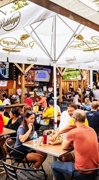 People dining at outdoor tables under umbrellas at a busy restaurant patio