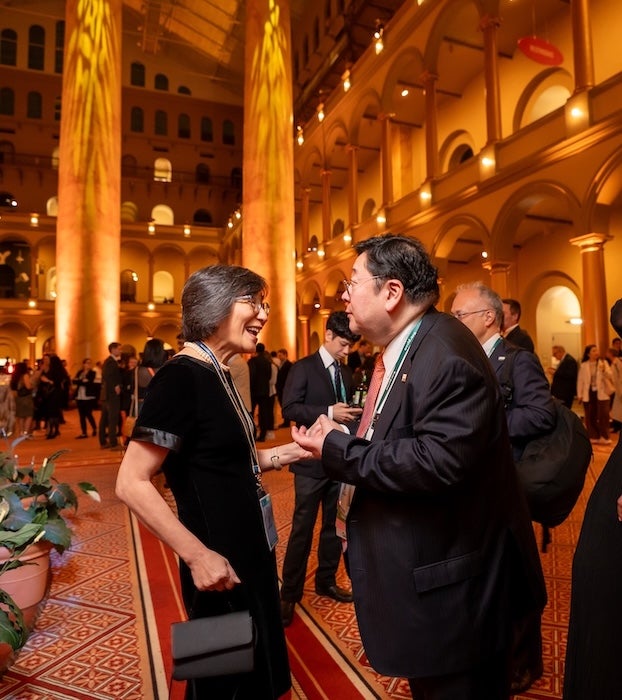 Photo of two people chatting in a grand, golden-lit hall during an evening event