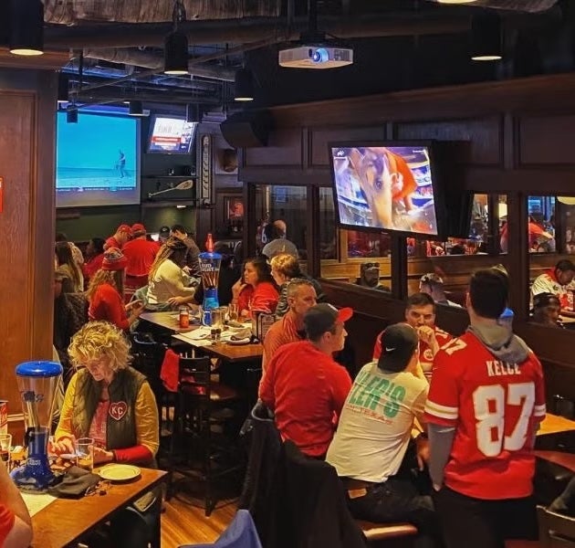 Sports bar packed with fans watching TVs, people in red jerseys at tables and bar