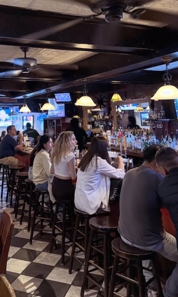 Crowded bar with people seated at high tables under warm pendant lights
