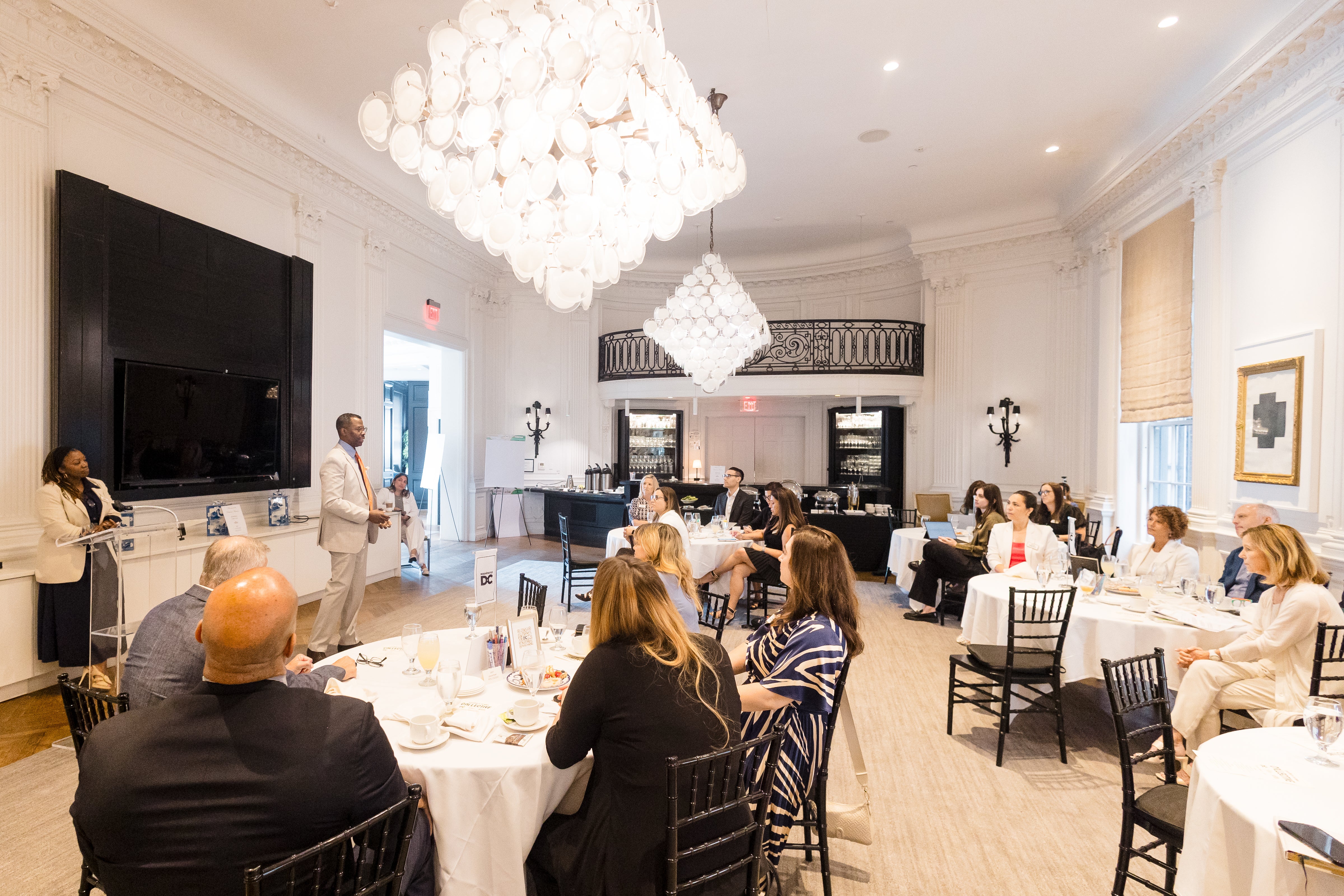 Photo of a bright private dining room with chandelier and guests at round tables