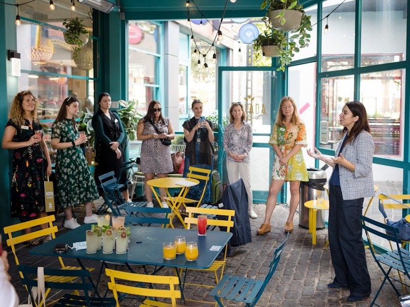 Photo of people gathered in a bright cafe with yellow chairs, listening to a speaker.