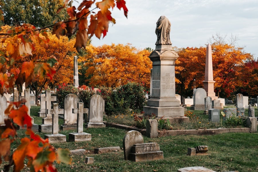 Cemetery headstones and a tall monument among orange fall trees