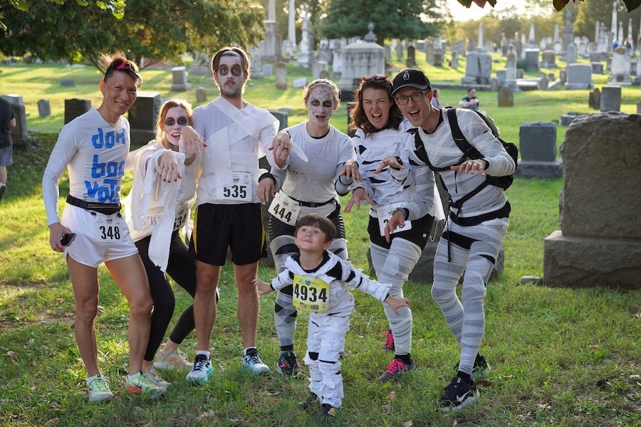 Runners posing in a cemetery dressed as mummies, one adult holding a small child in race bibs
