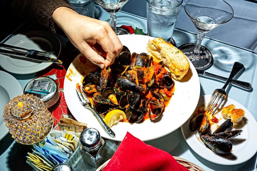Photo of mussels and bread on a table, person reaching in with a fork