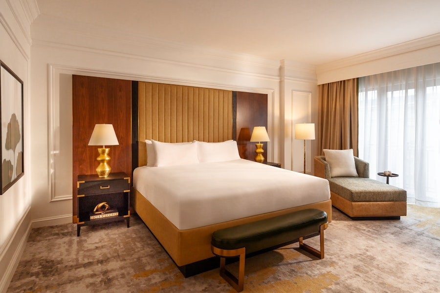 Modern hotel room with king bed, bench and lounge chair near window