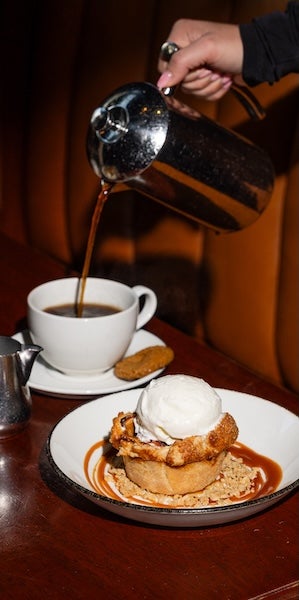 Person pouring coffee into a white cup beside pastries on a wooden table
