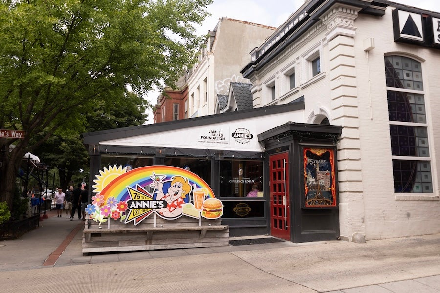Colorful mural on a white corner building with outdoor patio seating under awnings