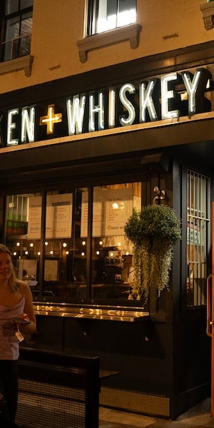 Photo of a warmly lit whiskey bar at night, glowing sign above windows and patio seating