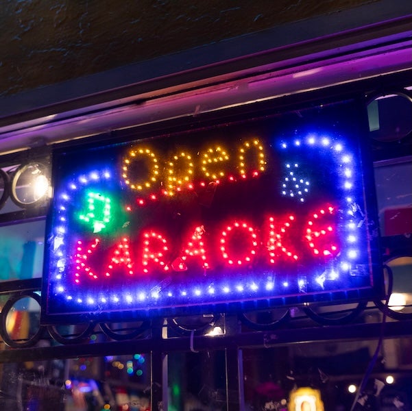 Neon sign reading “Open Karaoke” in blue, red and yellow lights at night