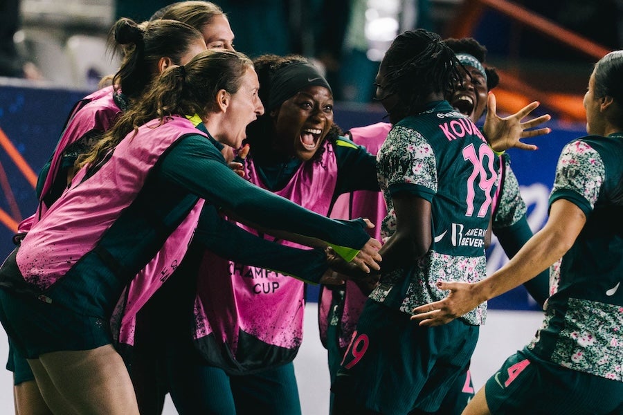 People in pink and blue jerseys celebrate on an indoor court, smiling and hugging