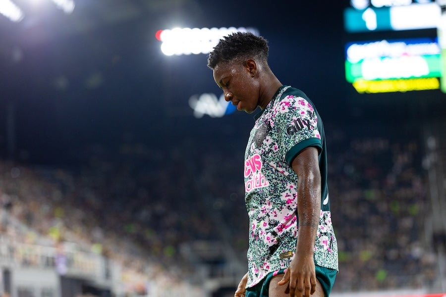 Soccer player in floral jersey walks with head down on a lit stadium field at night