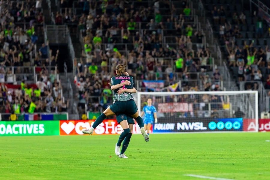 Photo of soccer player dribbling ball on field with packed stadium crowd