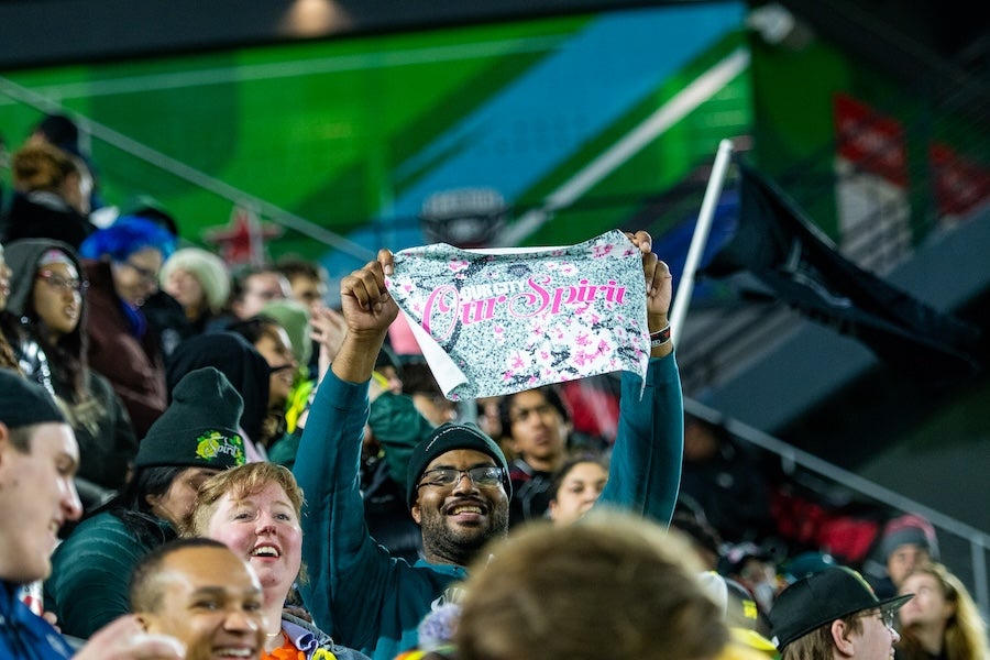 People cheering at a stadium, one holding a colorful sign up high