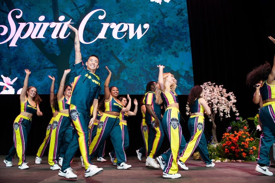 Spirit squad in green and yellow uniforms performs onstage under “Spirit Crew” banner