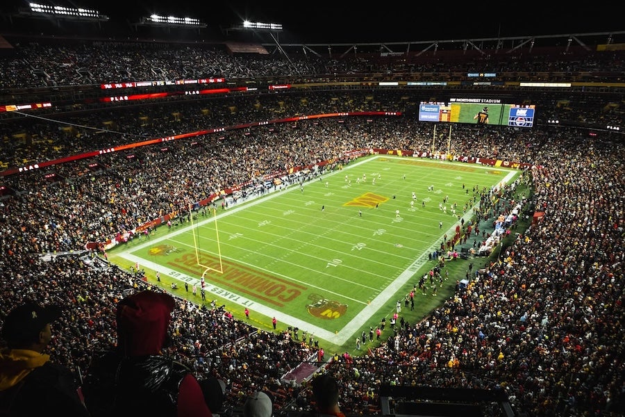 Packed football stadium at night, bright green field under lights