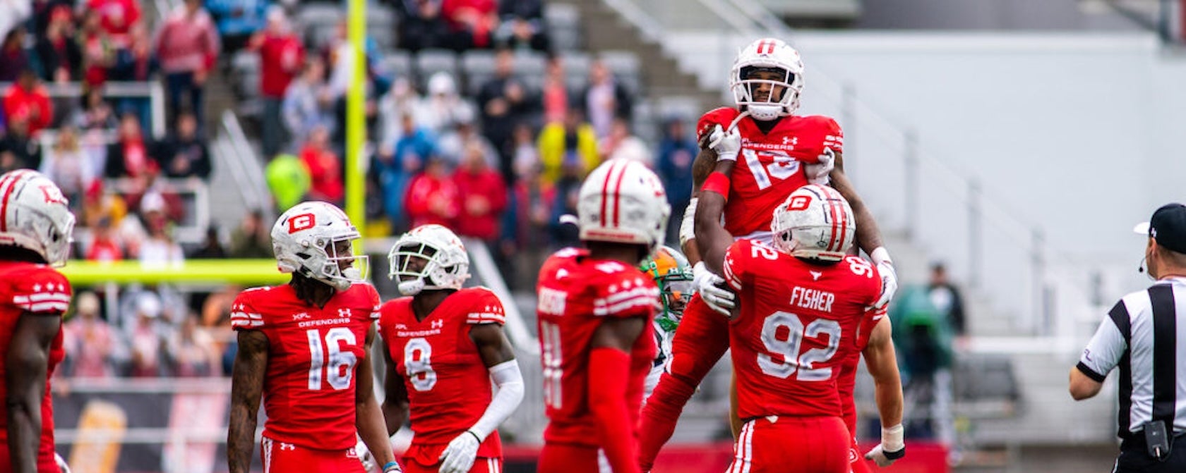 Photo, football players in red uniforms celebrate on the field as crowd watches.