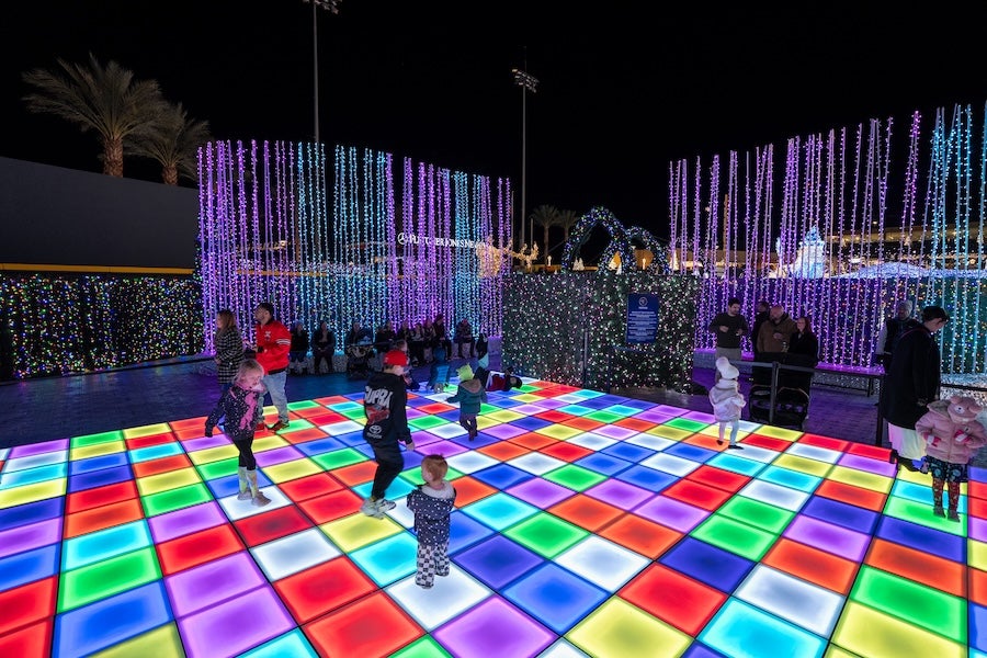 People dance on multicolor light-up floor under hanging light curtains at night.