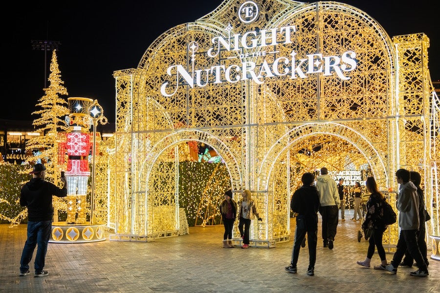 People walk under glowing Night of Nutcrackers arch at night.