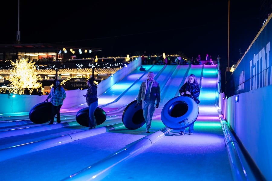 People relax in ring chairs on neon-lit rooftop at night, city skyline behind