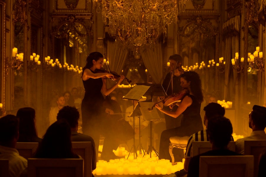 Candlelit chamber concert with string players onstage and seated audience in a golden hall