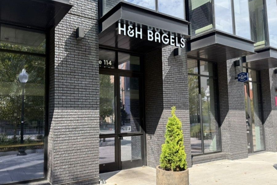Photo of H&H Bagels storefront with glass windows and a potted evergreen tree