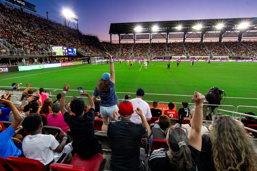 A night soccer match in a packed Audi Field as fans raise arms and cheer