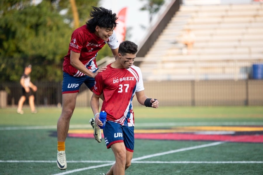 Two ultimate frisbee players in red jerseys celebrate on a field during a match